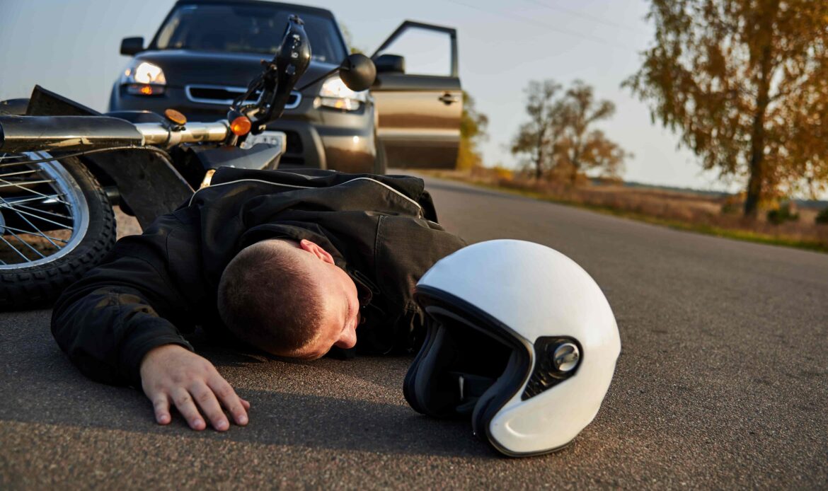 Motorcycle accident scene with injured rider lying on the road beside helmet and car. Motorcycle accident scene with injured rider lying on the road beside helmet and car.
