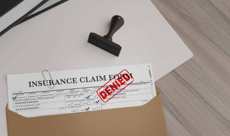 Insurance claim form stamped denied on desk with folder and rubber stamp.
