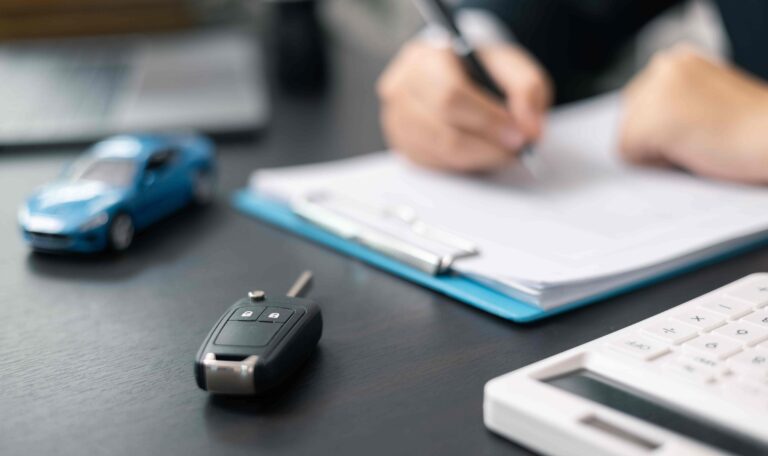 Person filling out car insurance claim form with car key and model car on desk.