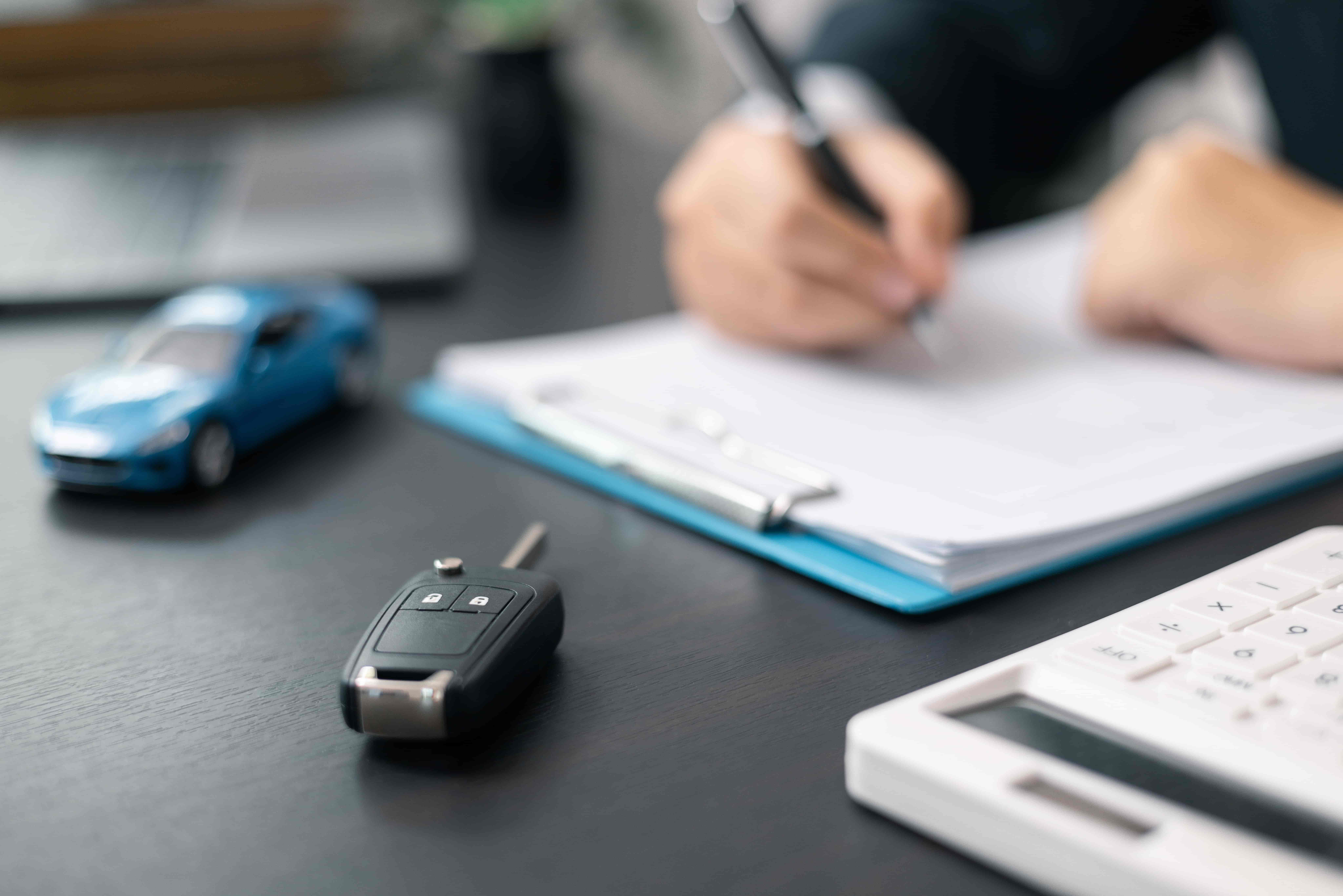 Person filling out car insurance claim form with car key and model car on desk. Person filling out car insurance claim form with car key and model car on desk.