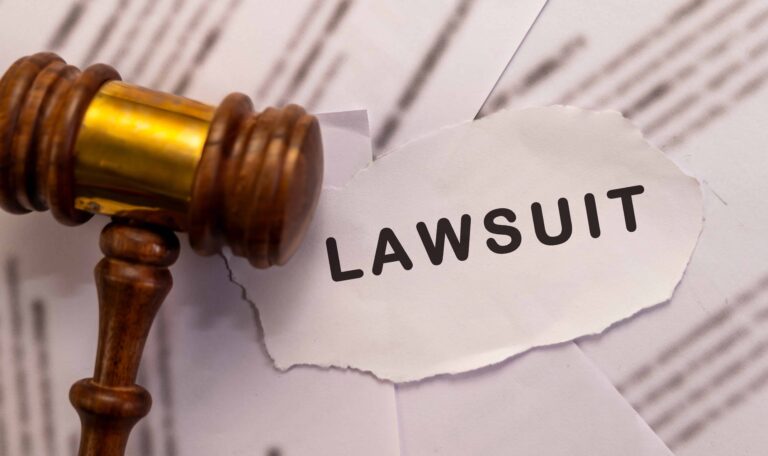 Judge’s gavel next to torn paper with the word lawsuit on legal documents.