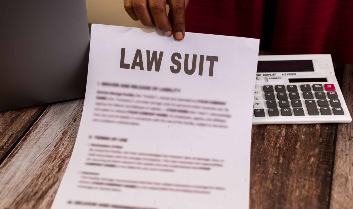 Person holding a lawsuit document with calculator on wooden desk.