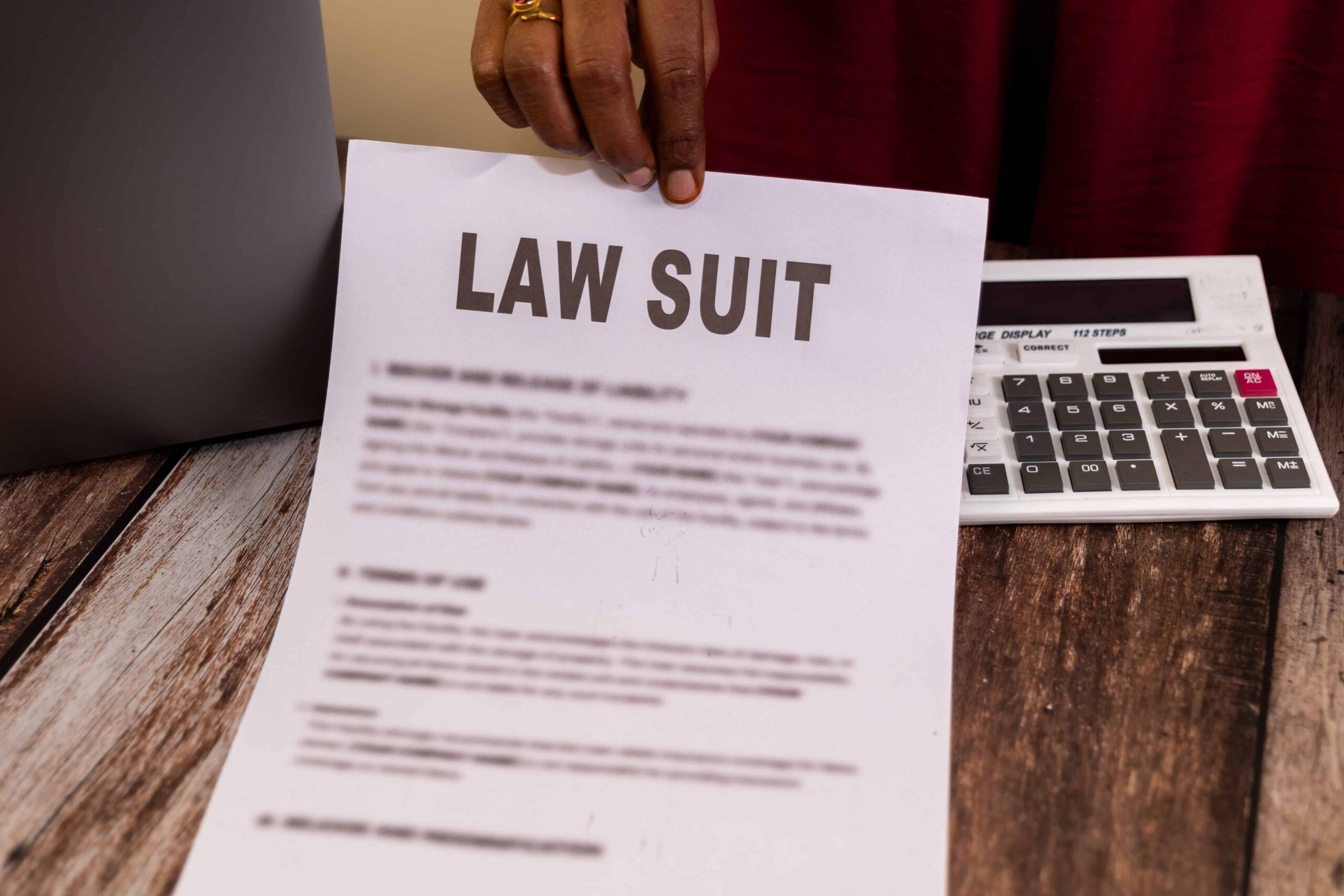 Person holding a lawsuit document with calculator on wooden desk. Person holding a lawsuit document with calculator on wooden desk.