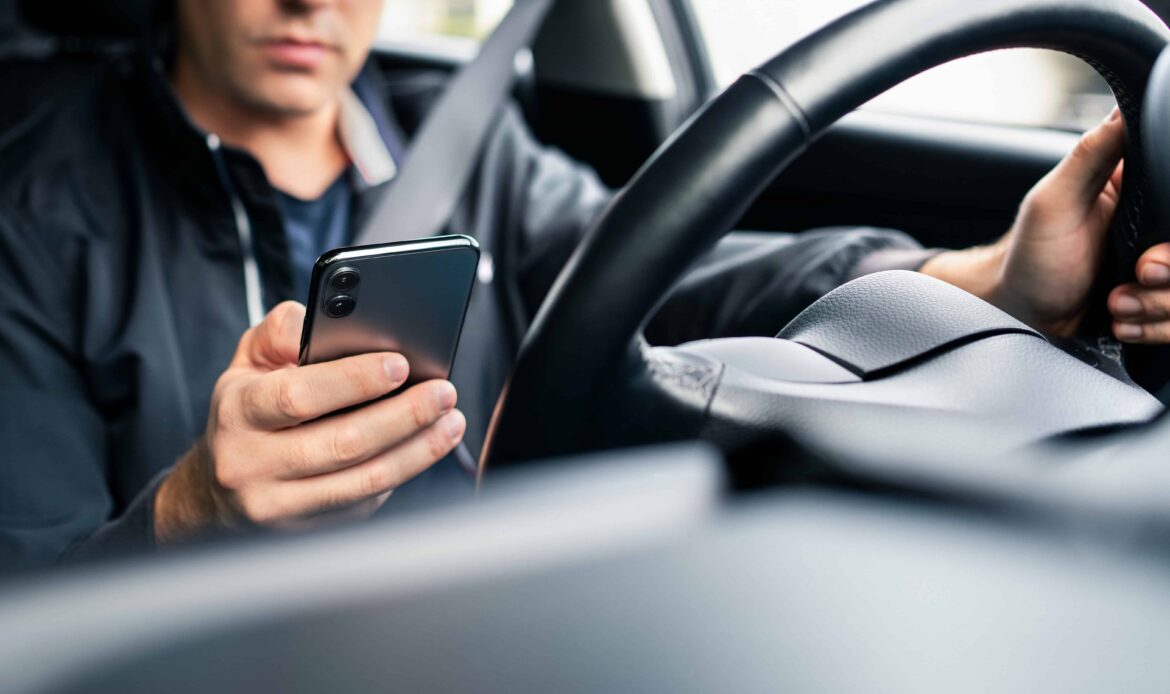 Driver texting on smartphone while behind the wheel, distracted driving concept.