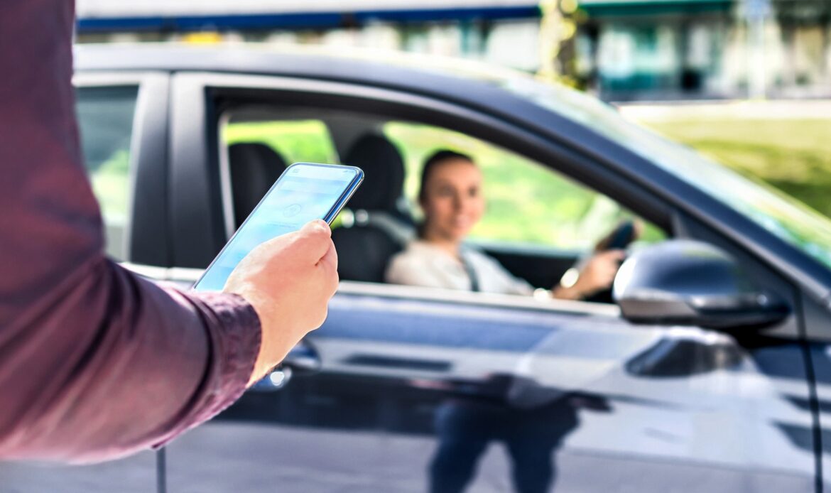 Person using smartphone to book a rideshare while driver waits in parked car.
