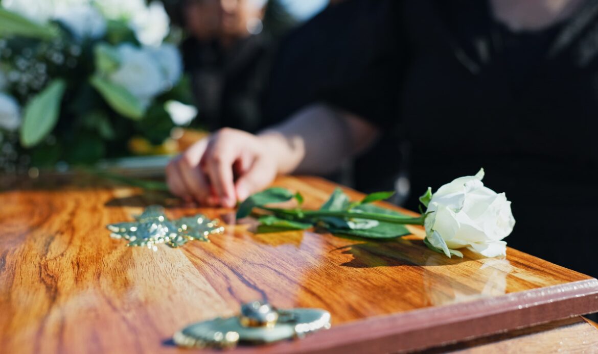 Mourner placing a white rose on a wooden casket during a funeral service Mourner placing a white rose on a wooden casket during a funeral service