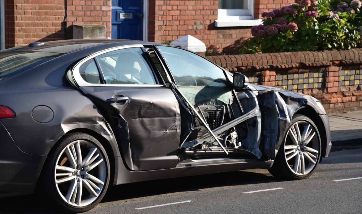 Car with severe side-impact damage and a crushed door after a collision on a residential street.