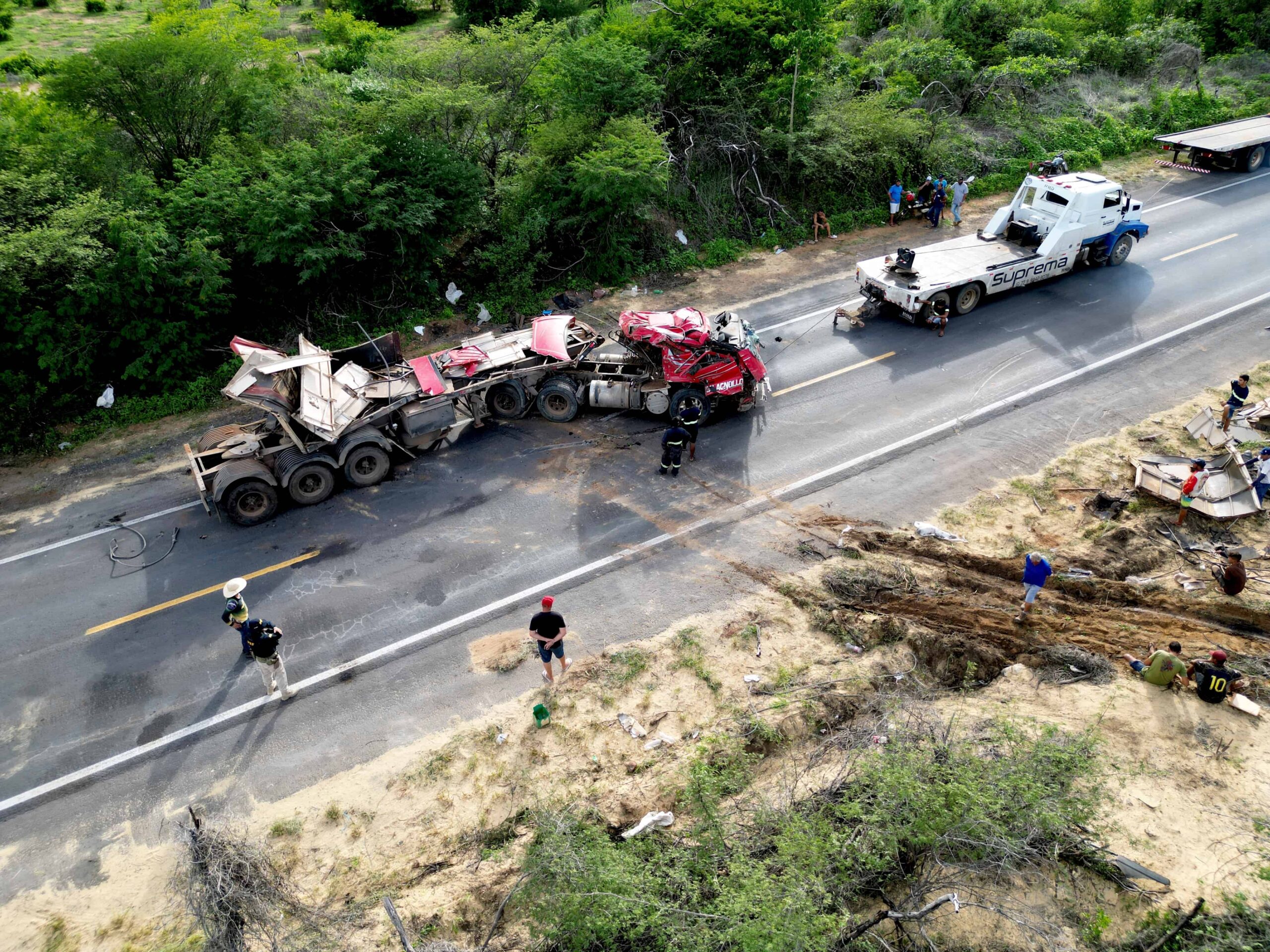 Aerial view of a serious semi-truck accident on a rural highway with emergency responders and tow trucks on scene.