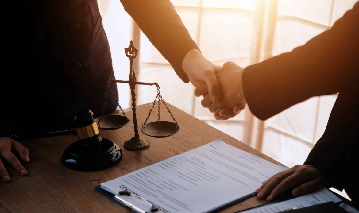 Two lawyers shaking hands over a legal agreement in an office with a gavel, balance scale, and contract documents on the desk. Two lawyers shaking hands over a legal agreement in an office with a gavel, balance scale, and contract documents on the desk.