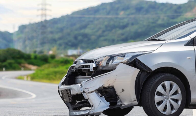 Front-end damage to a silver car after an accident on a rural road, representing auto collisions and vehicle crash claims.