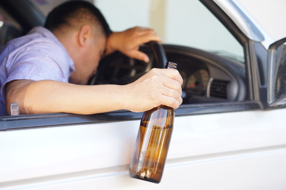 Intoxicated driver holding alcohol bottle in vehicle after leaving bar in Colorado
