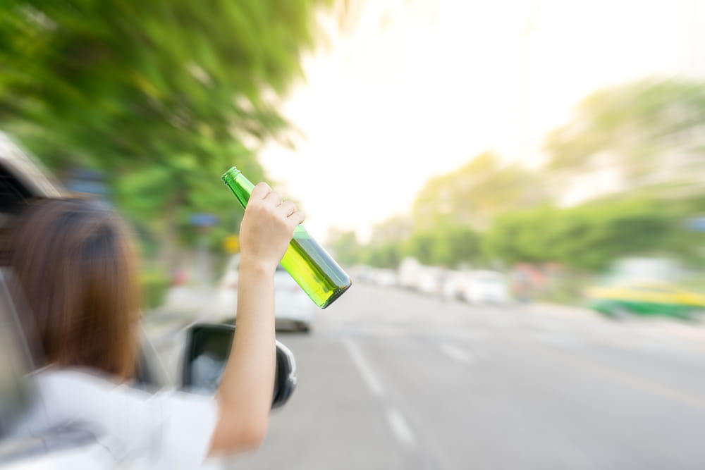 Underage driver holding alcohol bottle out of car window before DUI accident in Colorado