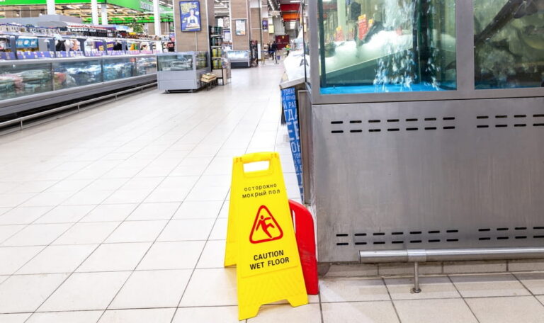 Caution wet floor sign in a grocery store aisle highlighting potential slip and fall hazard for customers