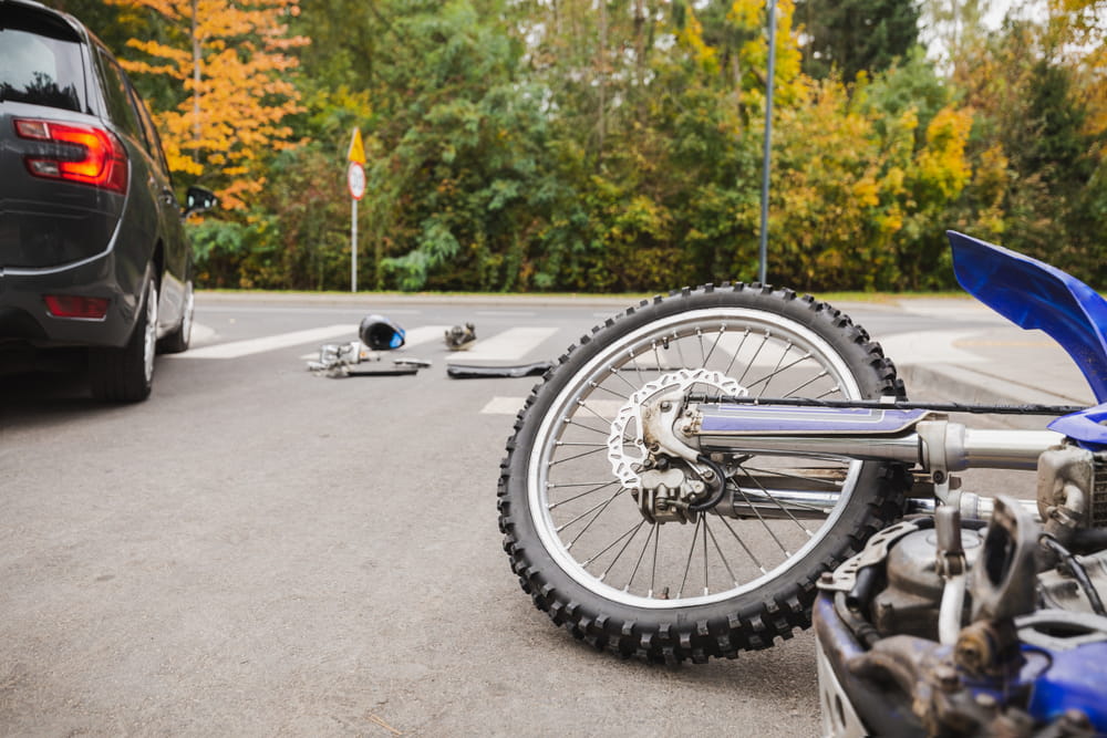 Motorcycle wreckage and dropped helmet at a crosswalk after a crash