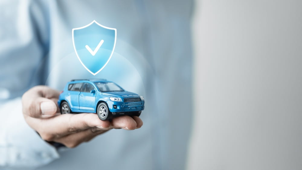Toy car held beneath a shield icon representing insurance coverage
