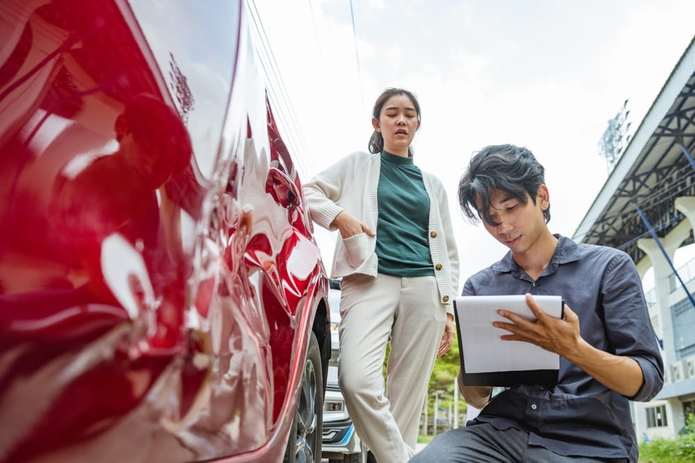 Insurance adjuster inspecting vehicle damage with clipboard after a car accident