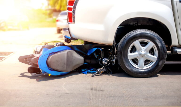 Motorcycle wreckage and dropped helmet at a crosswalk after a crash