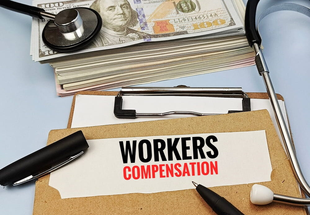 Clipboard labeled "Workers Compensation" with cash and a stethoscope