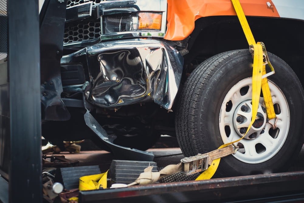 Damaged front end of a truck strapped to a tow flatbed after an accident